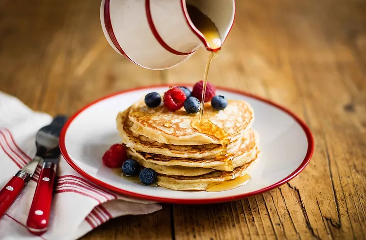 Pancakes with raspberries and blueberries and maple syrup being poured on them